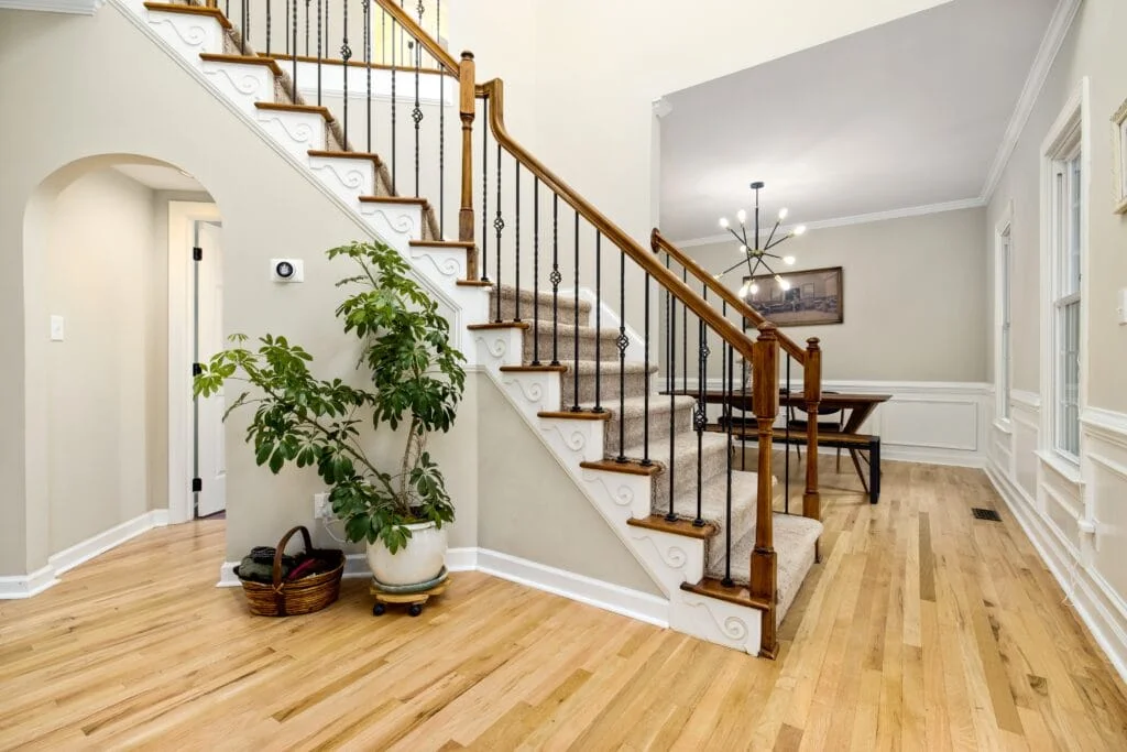 Classic home entryway with beautiful houseplants and iron banisters on the staircase